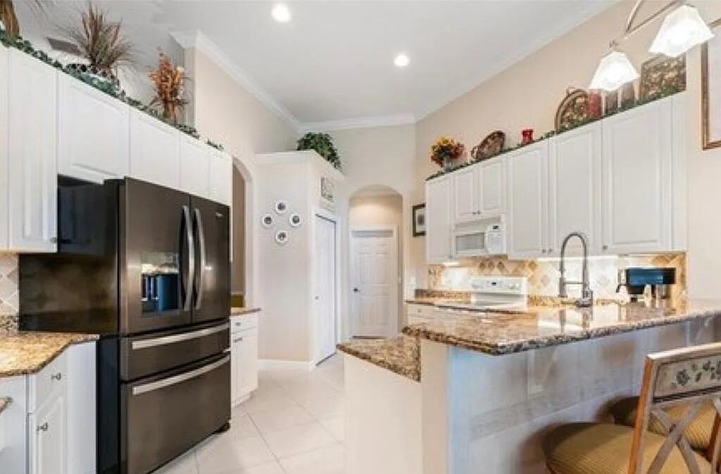 A kitchen with white cabinets, granite countertops, a dark refrigerator, and a breakfast bar — 4204 Abington Woods Circle, Vero Beach FL 32967, VERO BEACH, FL
