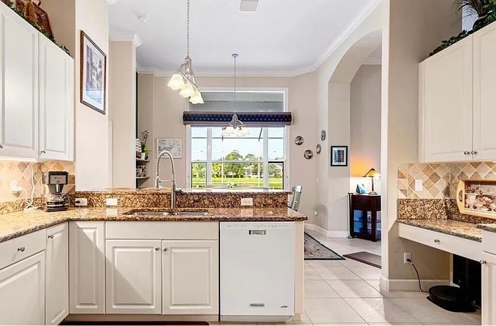 A kitchen with white cabinets, granite countertops, a dishwasher, and a view of a backyard — 4204 Abington Woods Circle, Vero Beach FL 32967, VERO BEACH, FL