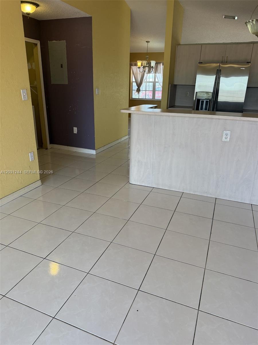 A kitchen with a breakfast bar, stainless steel refrigerator, and light-colored tile flooring — 13752 SW 156th St, Miami FL 33177, MIAMI, FL