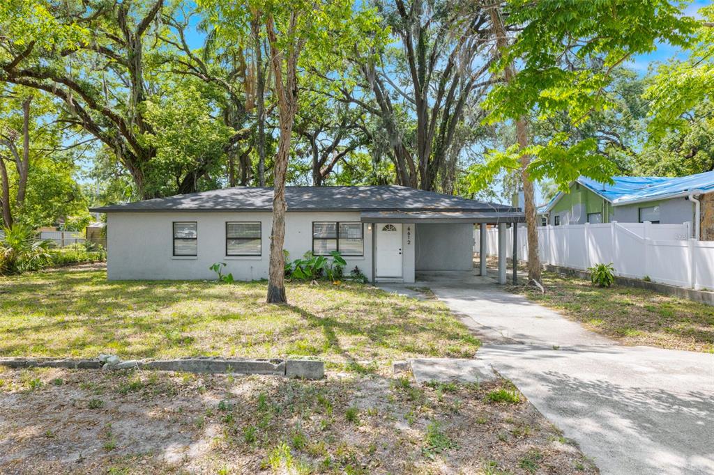 A single-story gray house with a carport sits on a grassy lot with large trees — 6612 N 23RD STREET, TAMPA, FL