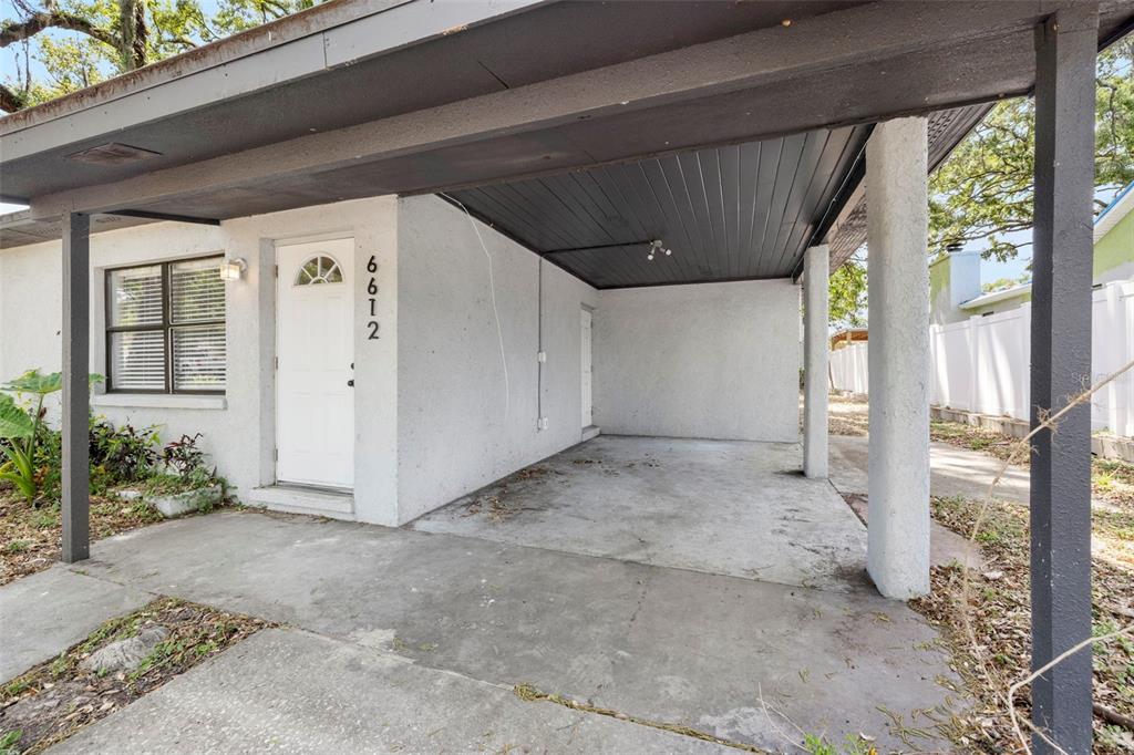 A white stucco house exterior features a front door and an attached concrete carport — 6612 N 23RD STREET, TAMPA, FL