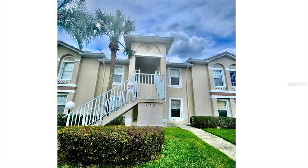 A two-story apartment building exterior features a central staircase leading to an upper-level entrance — 13415 FAIRWAY GLEN DRIVE UNIT 203, ORLANDO, FL