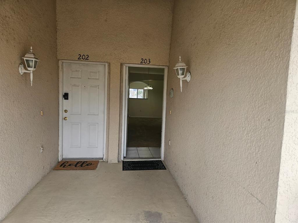 The exterior entryway shows two adjacent apartment doors numbered 202 and 203 with wall lamps — 13415 FAIRWAY GLEN DRIVE UNIT 203, ORLANDO, FL