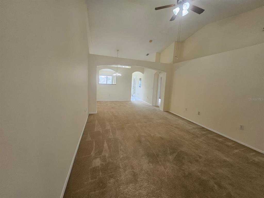 A carpeted living room with high ceilings and an arched entryway leads to a dining area — 13415 FAIRWAY GLEN DRIVE UNIT 203, ORLANDO, FL