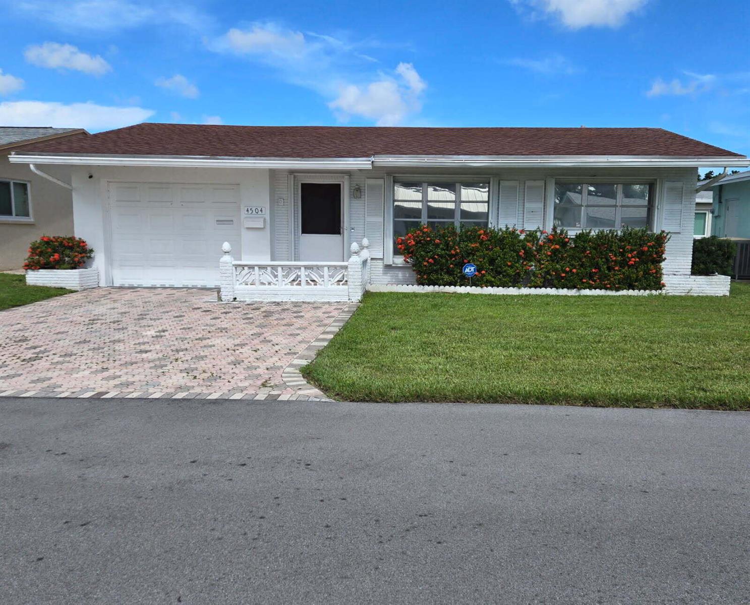 A single-story white house features a brick facade, a paved driveway, and a manicured lawn — 4504 NW 43rd Terrace, Tamarac FL 33319, TAMARAC, FL