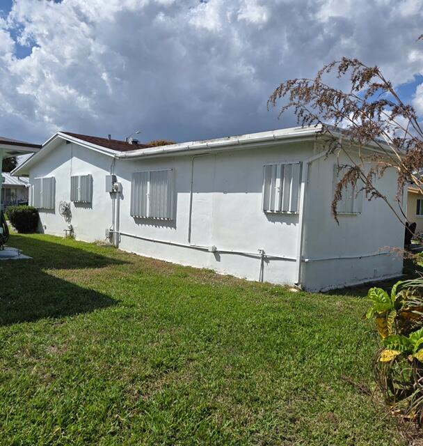 The exterior side view of a white, single-story house with metal hurricane shutters on windows — 4504 NW 43rd Terrace, Tamarac FL 33319, TAMARAC, FL