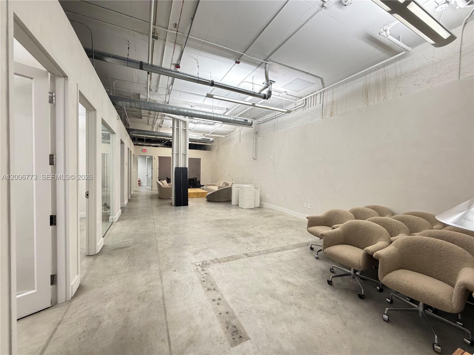 An industrial-style office space features concrete floors, exposed ceiling pipes, and several tan armchairs — 3015 Grand Ave # 0210, Miami FL 33133, MIAMI, FL