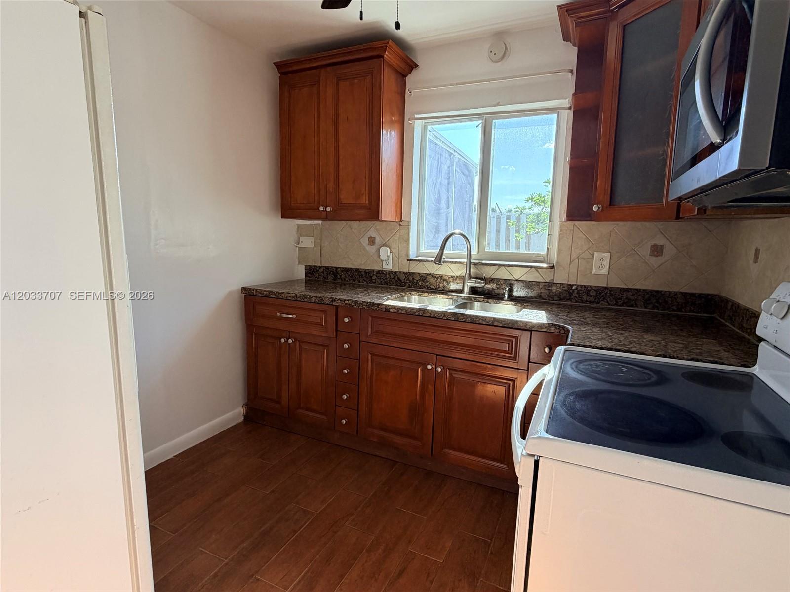 A kitchen features wood cabinets, granite countertops, a stainless steel sink, and wood-look tile flooring — 2500 Sunshine Blvd, Miramar FL 33023, MIRAMAR, FL