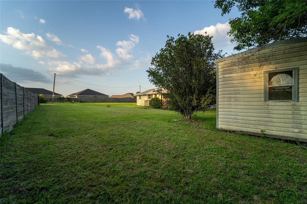 A grassy backyard features a storage shed, a large tree, and a wooden fence — 6915 KLONDIKE ROAD, PENSACOLA, FL