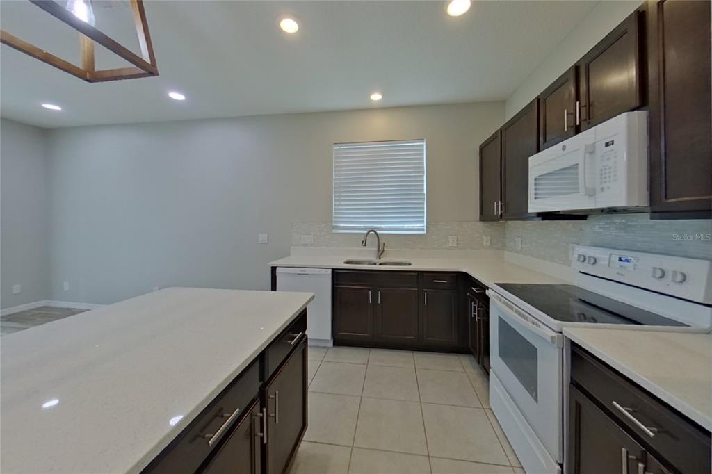 A kitchen features dark wood cabinets, white countertops, a white appliance suite, and tile flooring — 6317 DOMENICO COURT, GROVELAND, FL