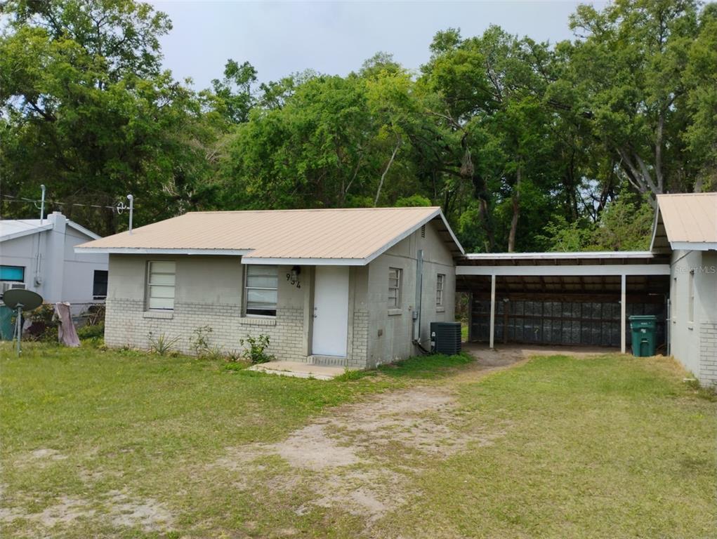 A single-story house with a light-colored brick exterior, a metal roof, and an attached carport — 934 NW 17TH AVENUE, OCALA, FL