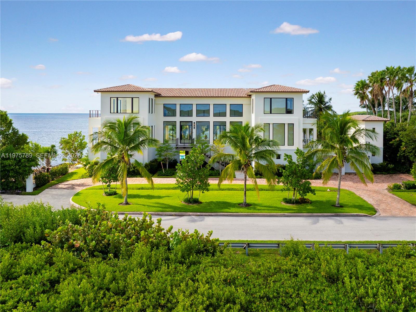 A large, multi-story Mediterranean-style house sits on a waterfront lot with palm trees — 650 Lugo Ave, Coral Gables FL 33156, CORAL GABLES, FL