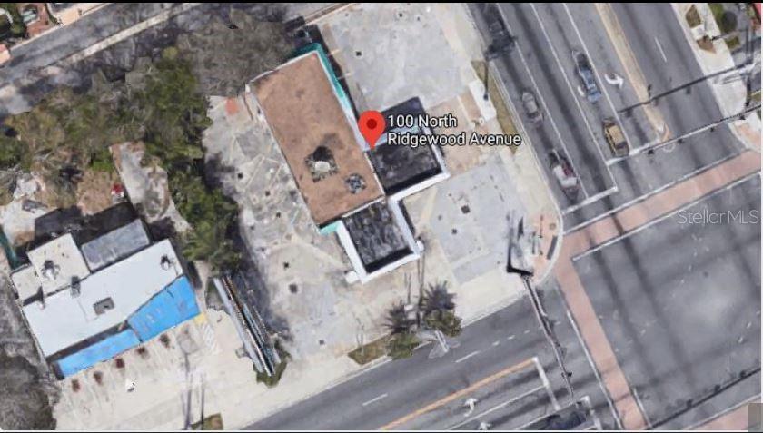 This aerial view shows a commercial building with a flat roof and surrounding parking lot — 100 N RIDGEWOOD AVENUE, DAYTONA BEACH, FL