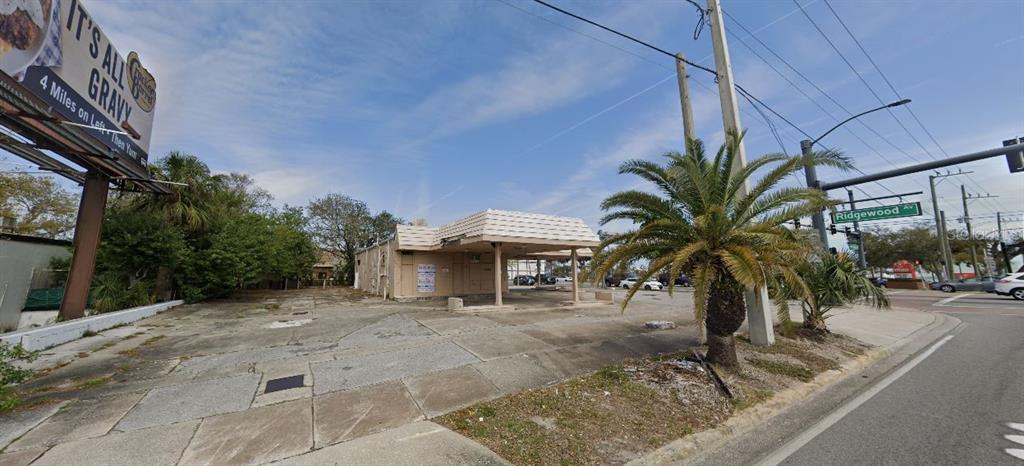 An exterior view of a vacant, single-story commercial building with a canopy and paved lot — 100 N RIDGEWOOD AVENUE, DAYTONA BEACH, FL