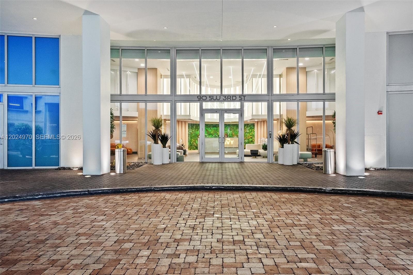 The exterior entrance of a modern building features a glass facade and a brick driveway — 90 SW 3rd St # 3810, Miami FL 33130, MIAMI, FL