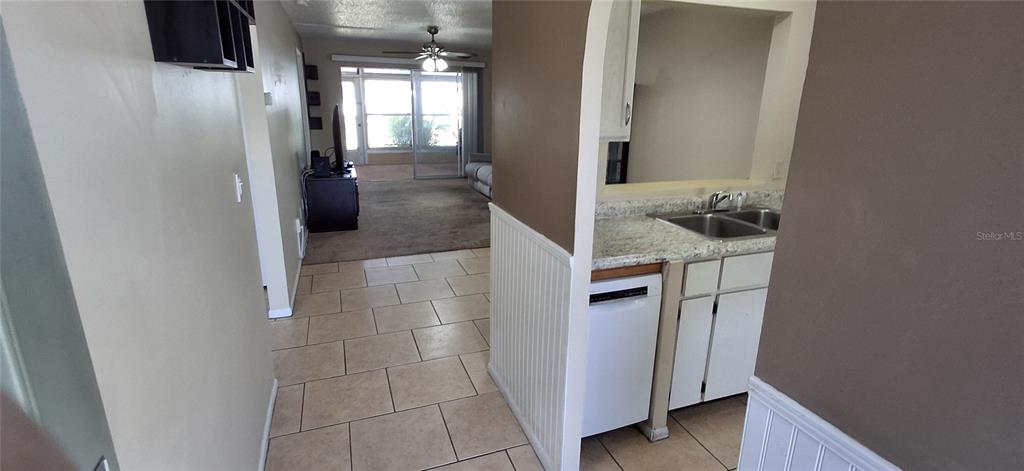 A kitchen with white cabinets and a dishwasher opens to a tiled living area — 4737 LAKE VILLA DRIVE, CLEARWATER, FL
