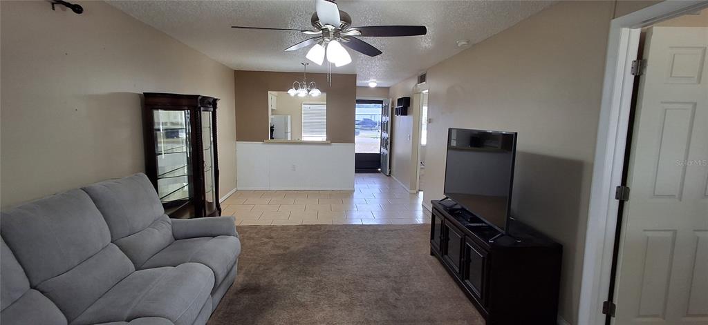 A living room with carpet, a sofa, a television, and an adjacent tiled dining area — 4737 LAKE VILLA DRIVE, CLEARWATER, FL