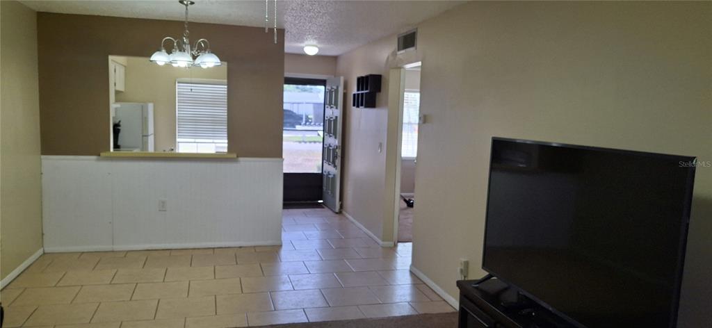 A living room with tile flooring, a kitchen pass-through, and an open front door — 4737 LAKE VILLA DRIVE, CLEARWATER, FL