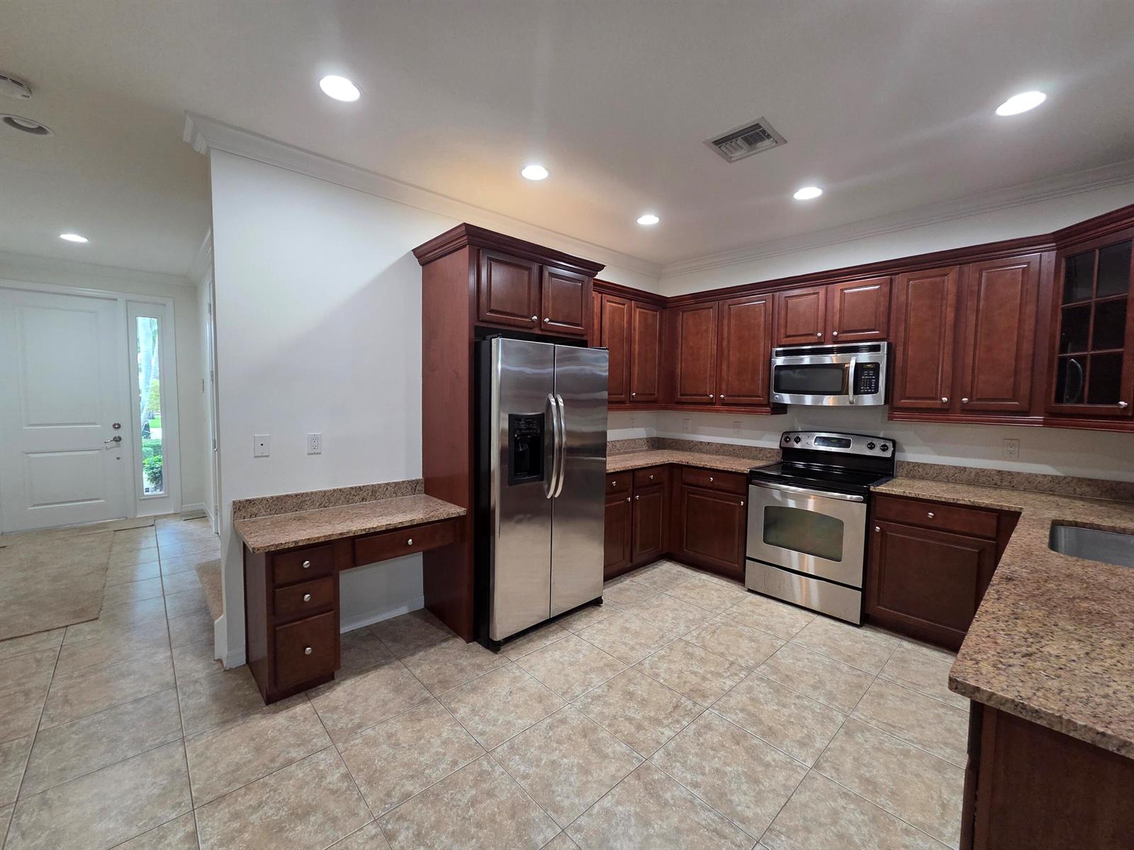 A kitchen features dark wood cabinets, stainless steel appliances, and granite countertops over tile flooring — 4507 Mediterranean Circle, West Palm Beach FL 33418, WEST PALM BEACH, FL