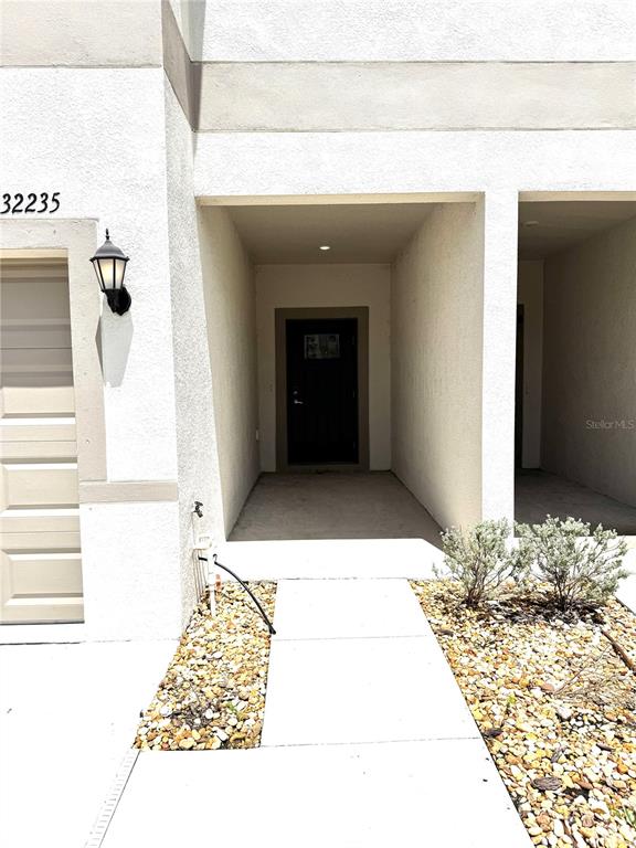 The exterior view shows a recessed entryway with a dark door next to a garage — 32235 POWDERPUFF MIMOSA DRIVE, SAN ANTONIO, FL