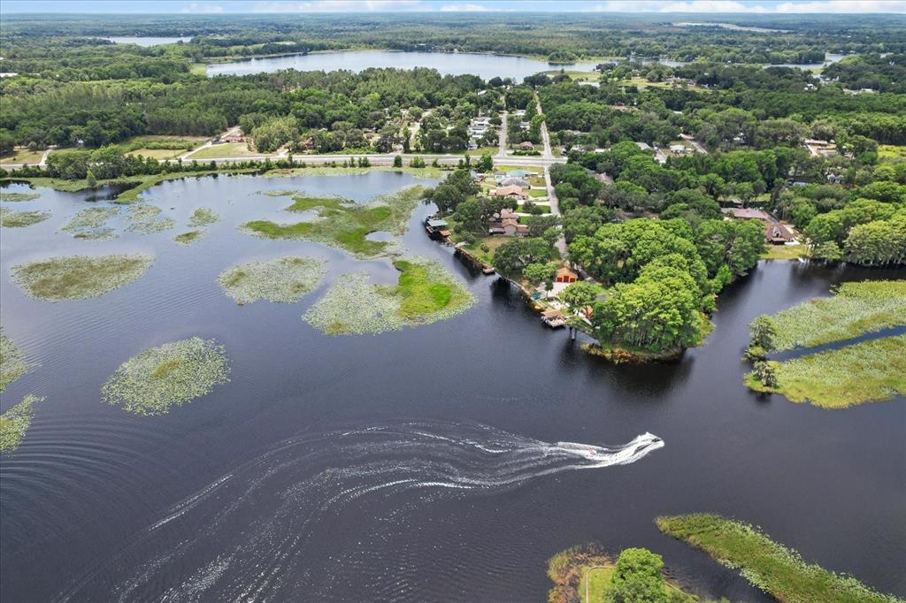 An aerial view shows a lake with lily pads, a boat, and surrounding residential properties — 1226 S TELEPHONE POINT ROAD, INVERNESS, FL