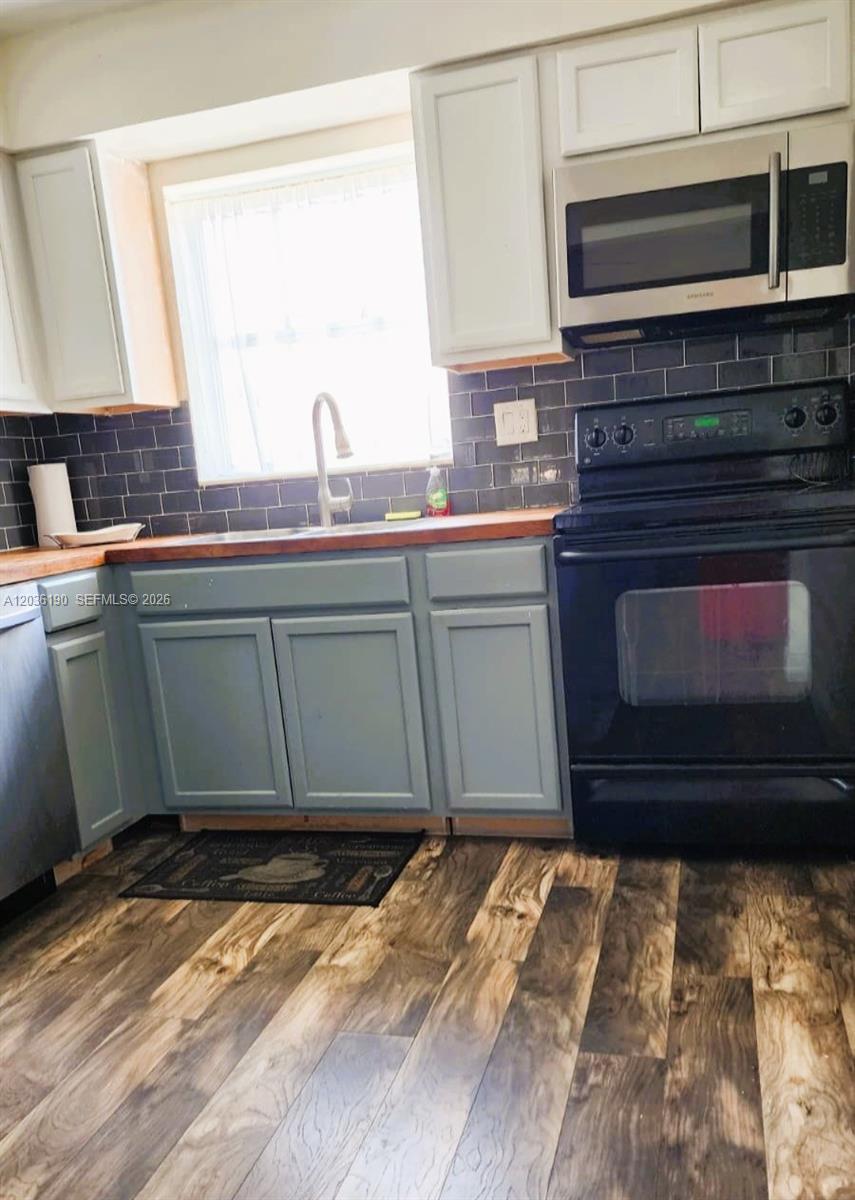 A kitchen features blue cabinets, a dark subway tile backsplash, and wood-look flooring — 2784 E Dudley Dr E, West Palm Beach FL 33415, WEST PALM BEACH, FL