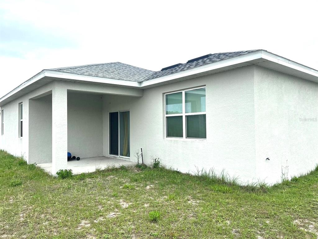 The exterior of a white stucco house features a covered patio and a sliding glass door — 305 ELDERBERRY COURT, POINCIANA, FL