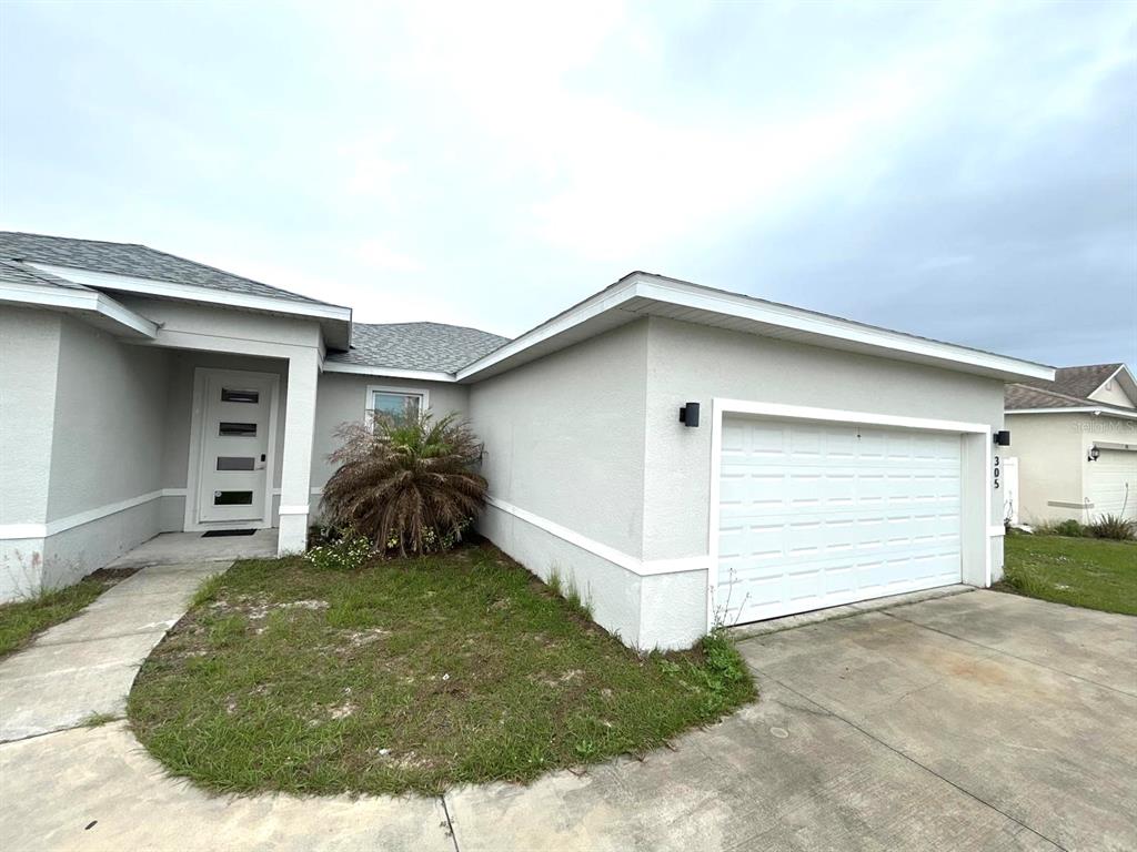 A single-story house exterior features a white garage door, a front entrance, and landscaping — 305 ELDERBERRY COURT, POINCIANA, FL