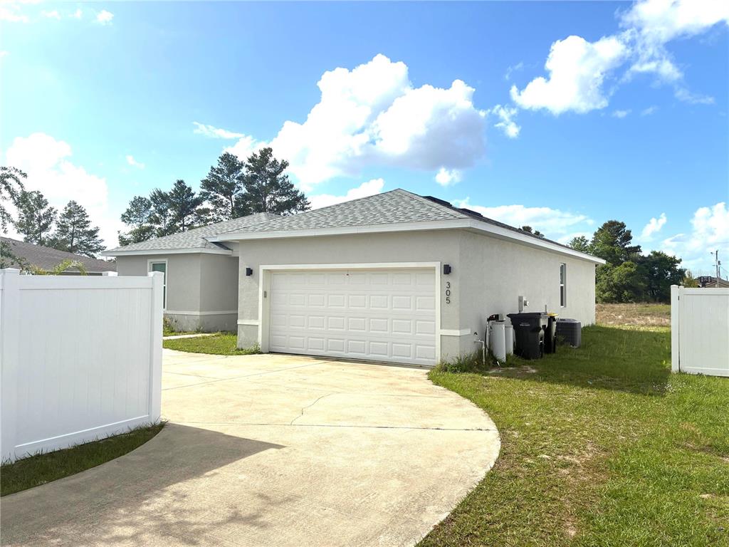 A single-story house with a white garage door, light-colored stucco exterior, and a concrete driveway — 305 ELDERBERRY COURT, POINCIANA, FL