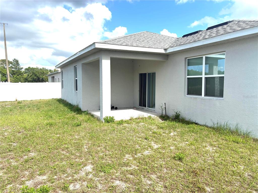 The exterior of a house features a covered concrete patio and a grassy backyard — 305 ELDERBERRY COURT, POINCIANA, FL