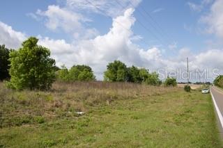 A grassy, undeveloped lot sits next to a paved road under a cloudy blue sky — KOKOMO ROAD NE, HAINES CITY, FL