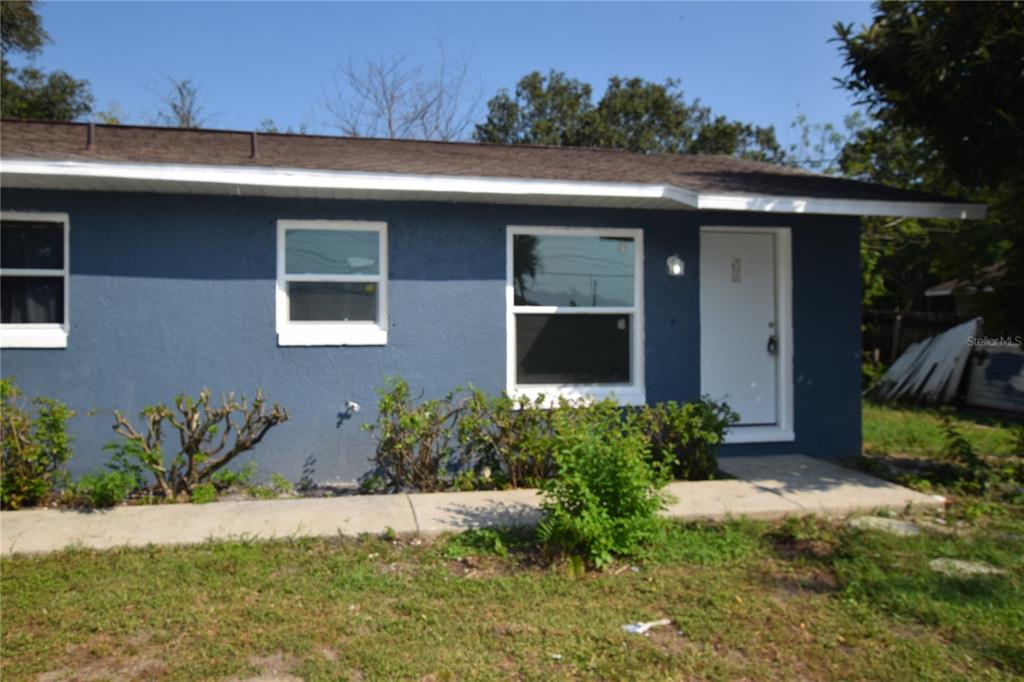 A blue single-story house exterior features a white front door, two windows, and landscaping — 911 NW 59TH COURT, OCALA, FL