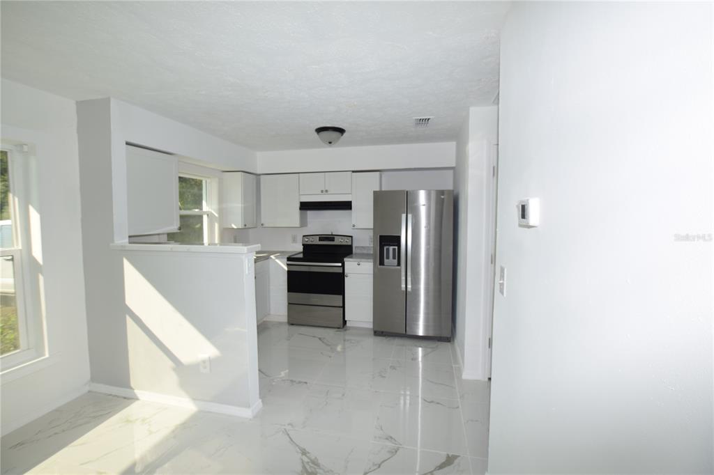 A kitchen features white cabinets, stainless steel appliances, and white marble-look tile flooring — 911 NW 59TH COURT, OCALA, FL