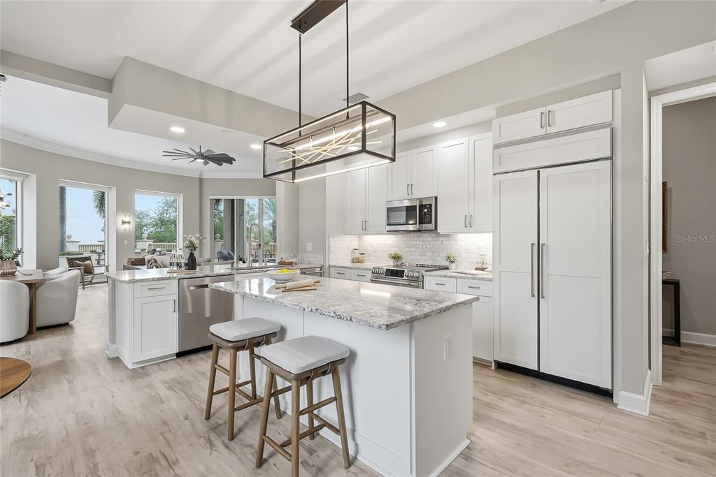 A modern kitchen features white cabinetry, a granite-topped island with stools, and stainless steel appliances — 100 BEACH DRIVE NE UNIT 301, ST PETERSBURG, FL