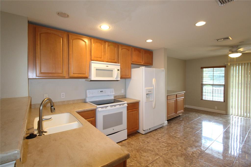 A kitchen with wood cabinets, white appliances, tan countertops, and tiled floors — 8828 WHITE SAGE LOOP, BRADENTON, FL