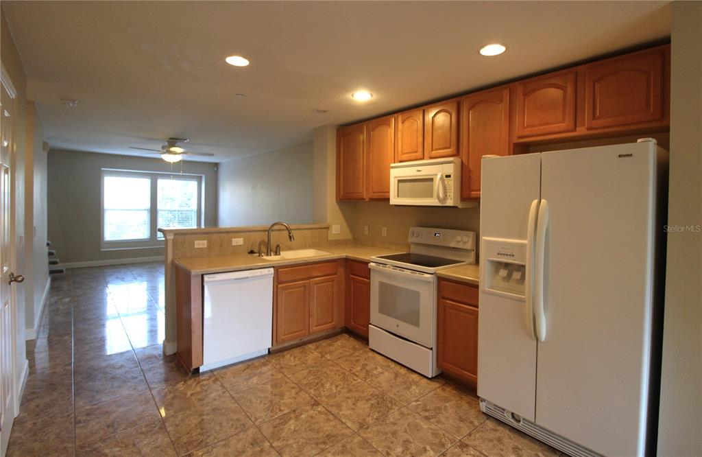 A kitchen with wood cabinets, white appliances, and tiled floors opens to a living area — 8828 WHITE SAGE LOOP, BRADENTON, FL