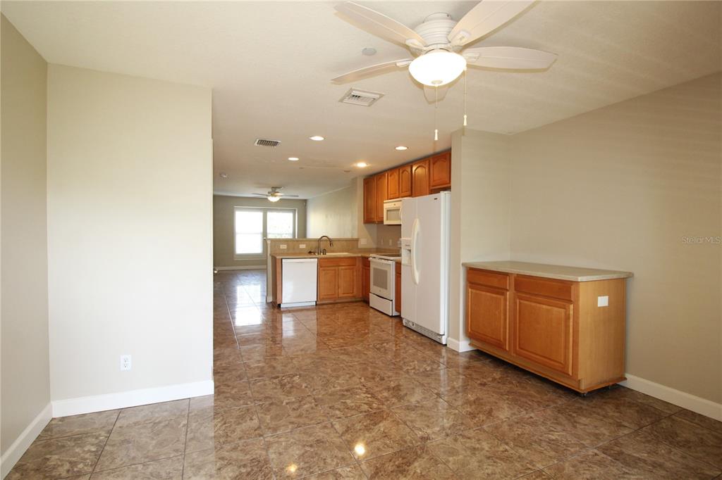 A kitchen with wood cabinets, white appliances, and brown tile flooring opens to a living area — 8828 WHITE SAGE LOOP, BRADENTON, FL