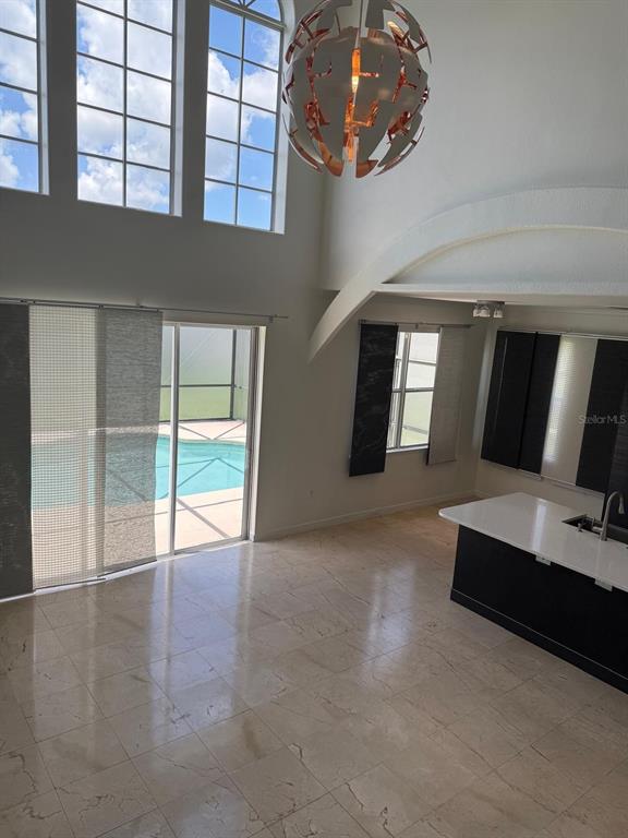 A high-ceilinged room with tile floors, a kitchen island, and sliding doors to a pool — 13406 MEADOW BAY LOOP, ORLANDO, FL