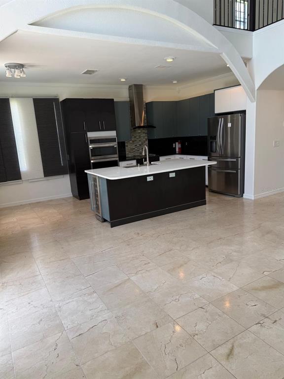 A modern kitchen features dark cabinetry, a white island countertop, and light-colored stone flooring — 13406 MEADOW BAY LOOP, ORLANDO, FL