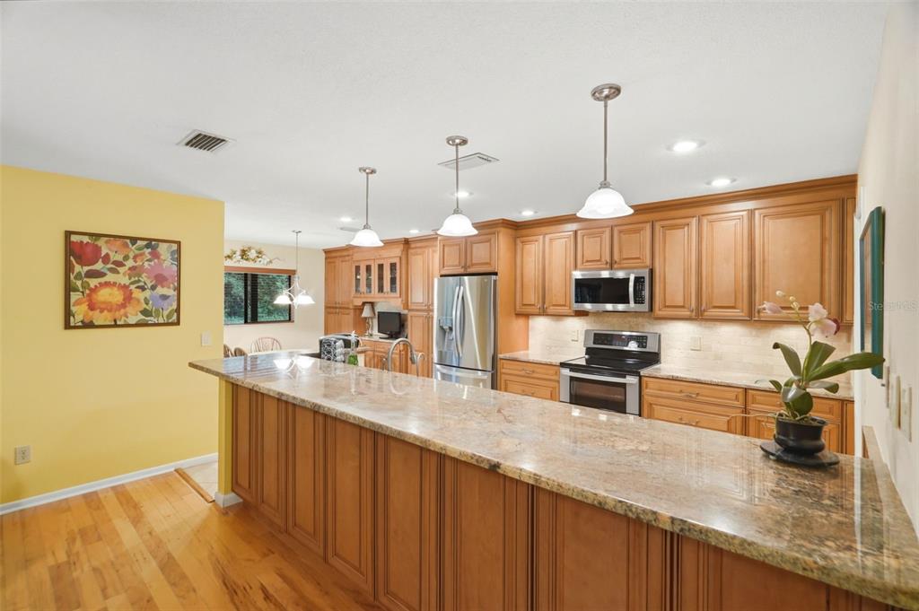A kitchen features wood cabinets, granite countertops, stainless steel appliances, and a breakfast bar — 1660 NARNIA COURT, DUNEDIN, FL