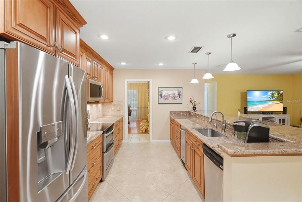 A kitchen with wood cabinets, granite countertops, stainless steel appliances, and a breakfast bar — 1660 NARNIA COURT, DUNEDIN, FL