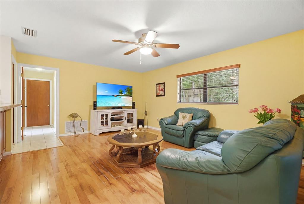 A living room with yellow walls, hardwood floors, a green sofa, and a ceiling fan — 1660 NARNIA COURT, DUNEDIN, FL
