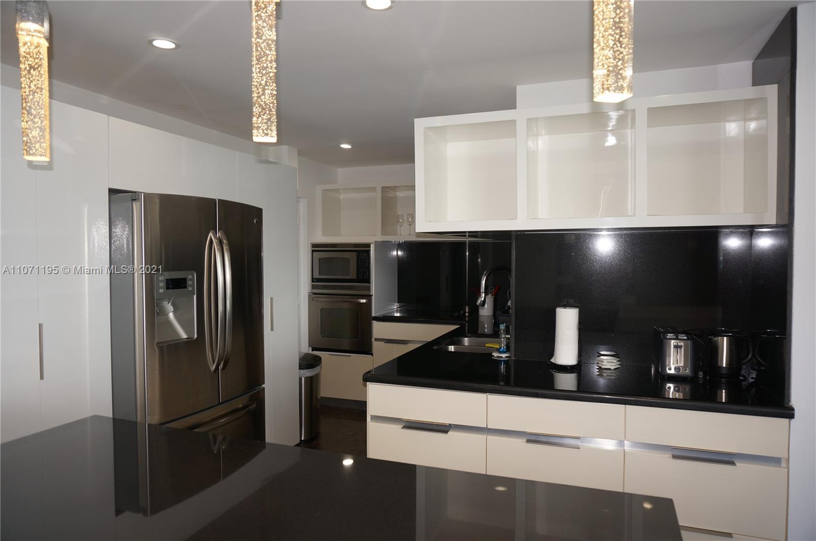 A modern kitchen features white cabinets, black countertops, stainless steel appliances, and pendant lighting — 4001 S Ocean Dr, Hollywood FL 33019, HOLLYWOOD, FL