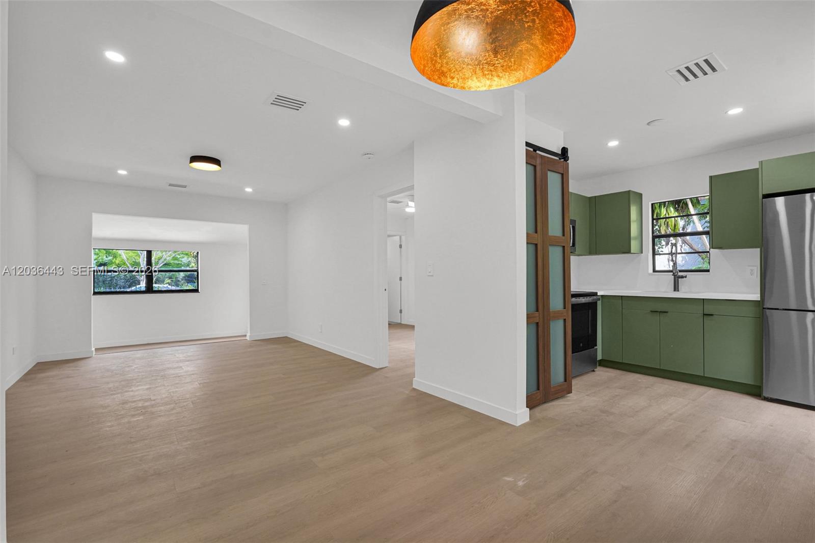 An open-concept kitchen with green cabinets and a sliding barn door leads to a living area — 81 NW 45th St # 0, Miami FL 33127, MIAMI, FL
