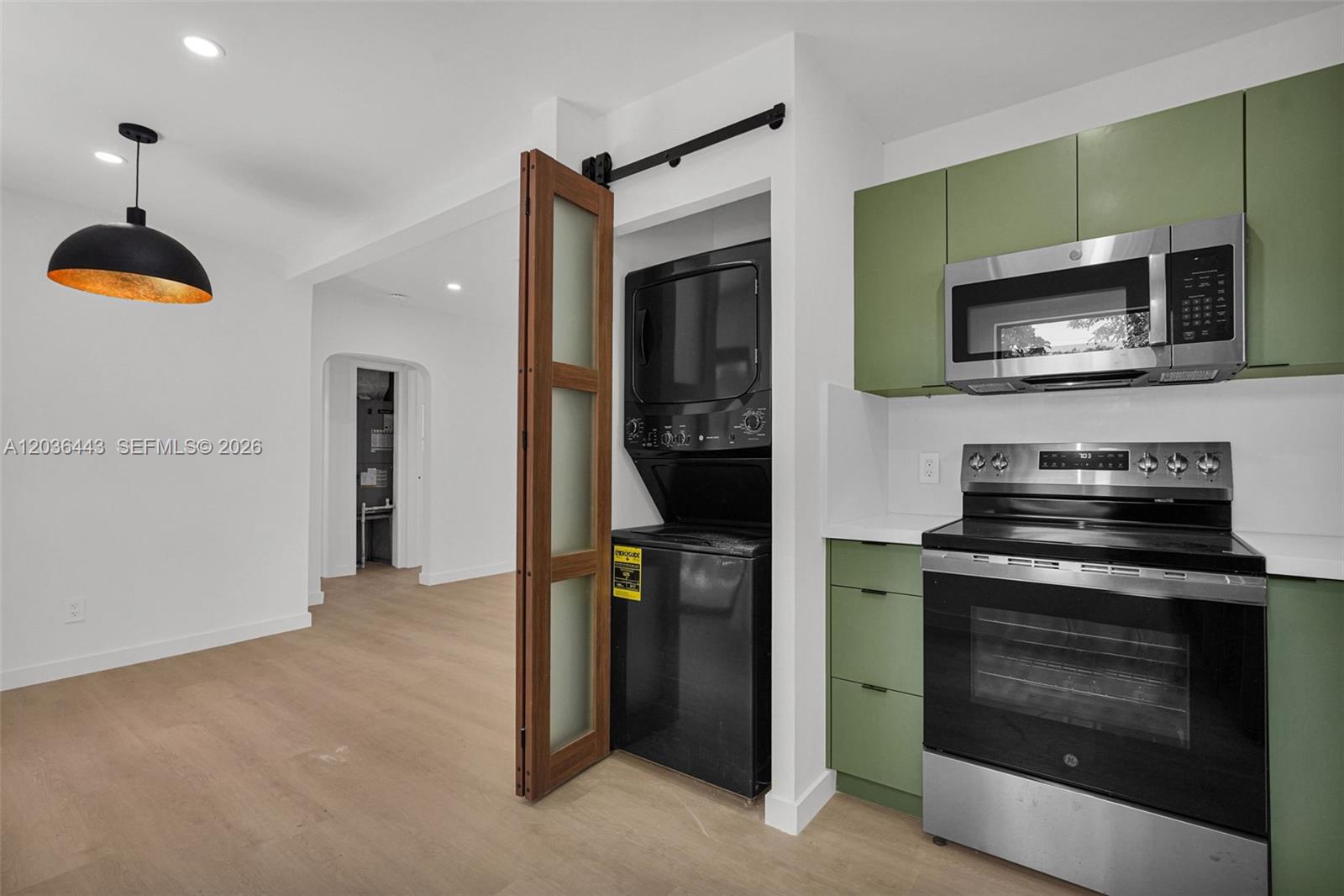 A kitchen features green cabinets, stainless steel appliances, and a stacked washer-dryer behind barn doors — 81 NW 45th St # 0, Miami FL 33127, MIAMI, FL