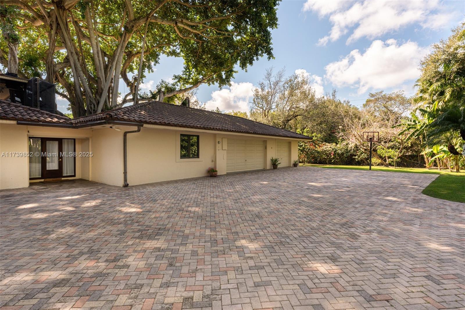 A paved driveway leads to a house with a multi-car garage and a large tree — 9490 Old Cutler Ln, Coral Gables FL 33156, CORAL GABLES, FL