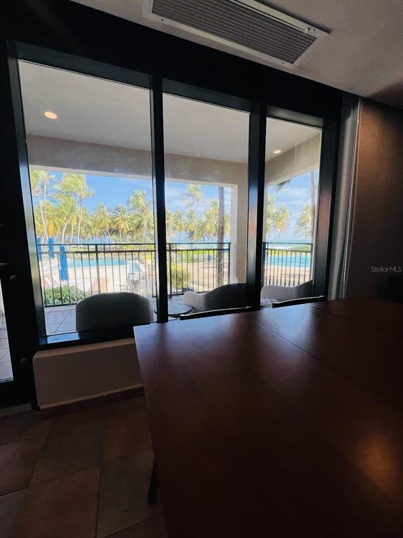 A dining room with a large wooden table overlooks a balcony, pool, and palm trees — OCEAN VILLAS I 6000 BLVD. RIO MAR UNIT /, RIO GRANDE, PR