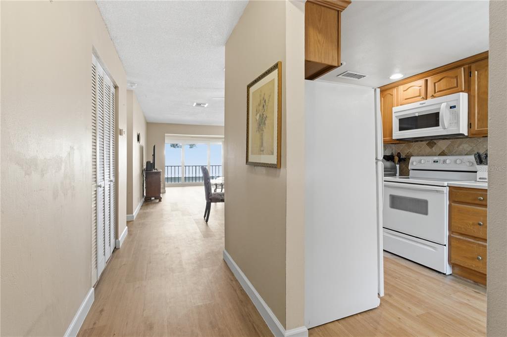 A hallway leads from a kitchen with white appliances toward a dining area with balcony access — 2060 MARILYN STREET UNIT 207, CLEARWATER, FL