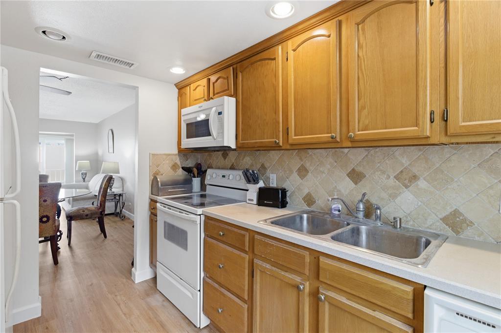 A kitchen features wood cabinets, a white stove, a microwave, and a tiled backsplash — 2060 MARILYN STREET UNIT 207, CLEARWATER, FL