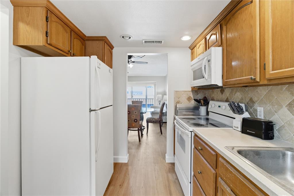 A galley kitchen features wood cabinets, white appliances, and a tiled backsplash — 2060 MARILYN STREET UNIT 207, CLEARWATER, FL
